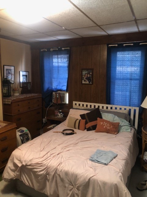 bedroom featuring a drop ceiling, wood walls, and cooling unit