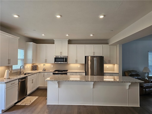 kitchen featuring dark wood-type flooring, stainless steel appliances, sink, a center island, and white cabinetry