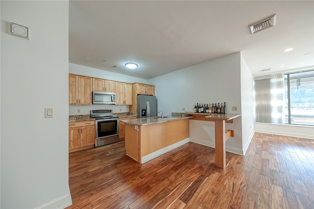 kitchen featuring kitchen peninsula, a breakfast bar area, light stone countertops, dark wood-type flooring, and stainless steel appliances