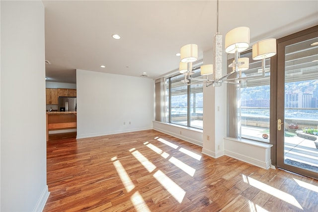 unfurnished dining area with a notable chandelier, wood-type flooring, and plenty of natural light