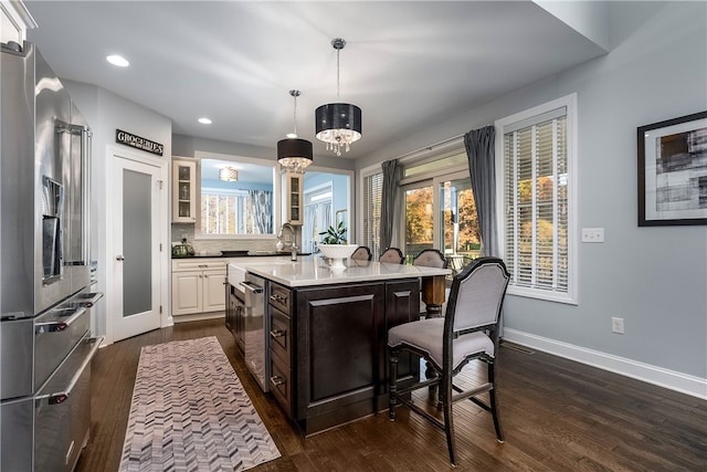 kitchen featuring dark brown cabinets, a center island with sink, appliances with stainless steel finishes, dark wood-type flooring, and decorative light fixtures