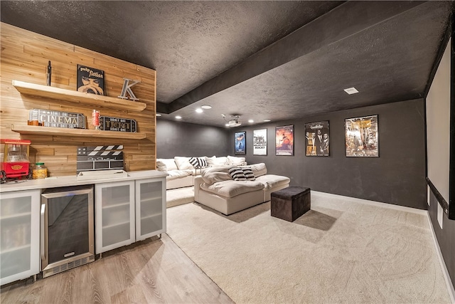 cinema room featuring a textured ceiling, indoor bar, beverage cooler, and light wood-type flooring