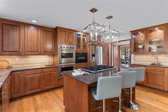 kitchen with a kitchen breakfast bar, dark stone counters, a center island, light wood-type flooring, and appliances with stainless steel finishes