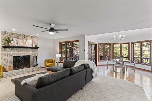 living room with light wood-type flooring, a wealth of natural light, a brick fireplace, and ceiling fan with notable chandelier