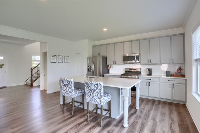 kitchen featuring a breakfast bar area, a center island with sink, light wood-type flooring, gray cabinets, and appliances with stainless steel finishes