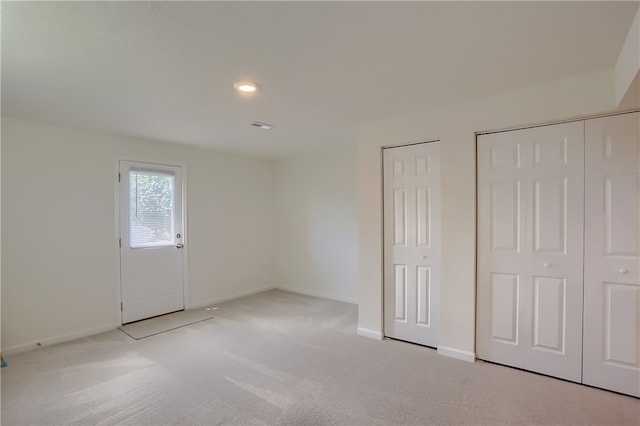 unfurnished bedroom featuring multiple closets and light colored carpet