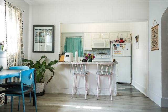 kitchen with tasteful backsplash, white appliances, light hardwood / wood-style flooring, white cabinets, and a breakfast bar area