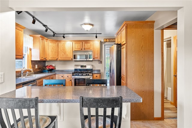 kitchen featuring sink, track lighting, a kitchen bar, and stainless steel appliances