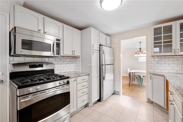 kitchen with backsplash, light stone countertops, white cabinetry, light tile patterned floors, and appliances with stainless steel finishes