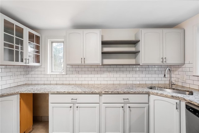 kitchen featuring stainless steel dishwasher, sink, white cabinets, and light stone counters