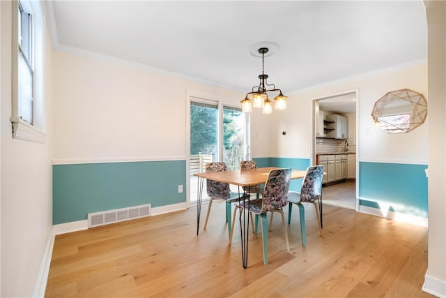 dining area featuring an inviting chandelier, ornamental molding, sink, and light hardwood / wood-style floors