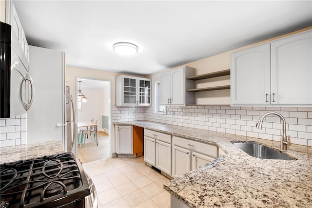 kitchen with gas range, white cabinetry, light stone countertops, and sink