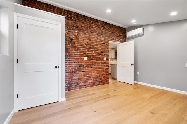 empty room featuring an AC wall unit, brick wall, and light wood-type flooring