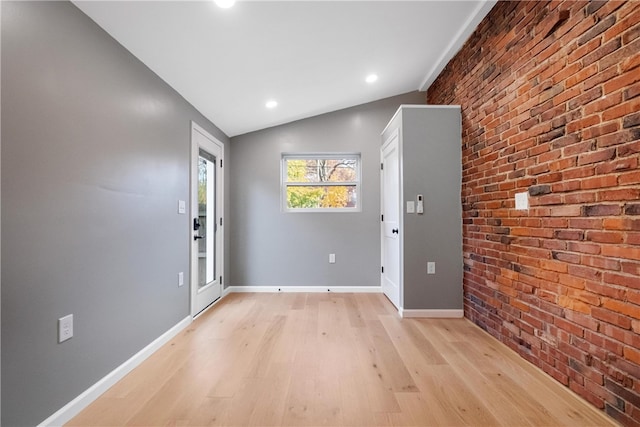 entryway with brick wall, vaulted ceiling, and light hardwood / wood-style flooring