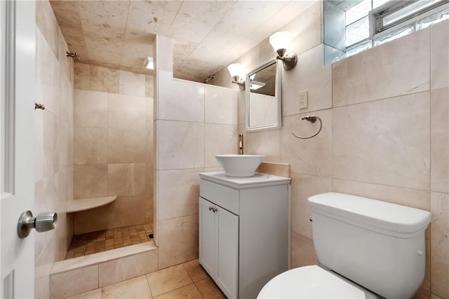 bathroom featuring a tile shower, tile walls, toilet, vanity, and tile patterned floors