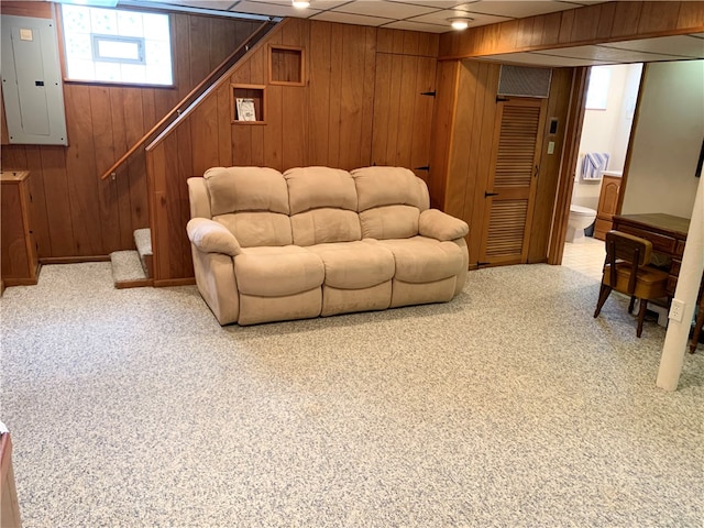 living room with wood walls, carpet flooring, electric panel, and a drop ceiling