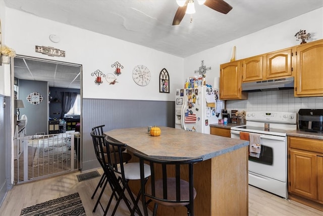 kitchen with ceiling fan, backsplash, a breakfast bar, light wood-type flooring, and white appliances