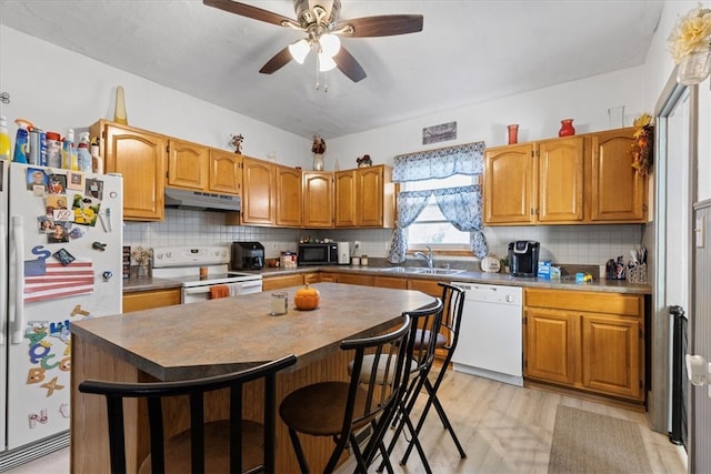 kitchen with white appliances, sink, a kitchen bar, and a kitchen island