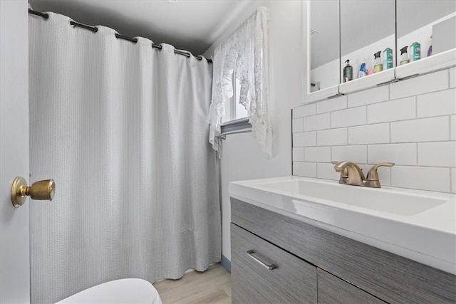 bathroom featuring backsplash, walk in shower, hardwood / wood-style flooring, toilet, and vanity