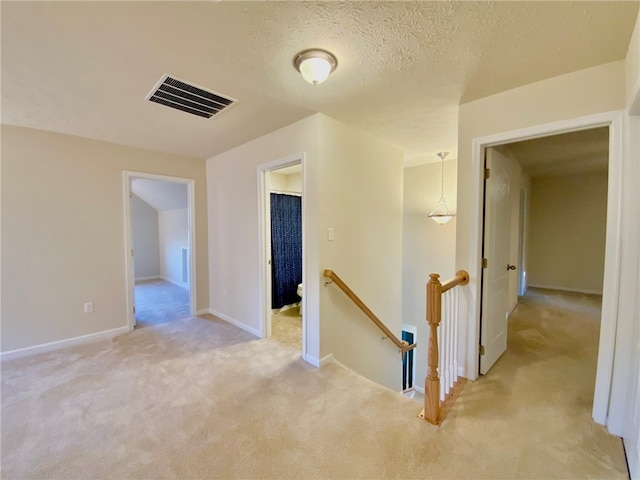 corridor with a textured ceiling and light colored carpet