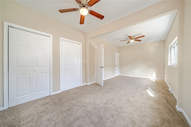 unfurnished bedroom with two closets, carpet floors, and ceiling fan