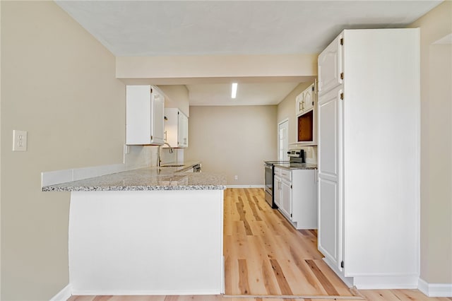 kitchen with stainless steel electric range, white cabinets, light stone counters, light hardwood / wood-style flooring, and sink