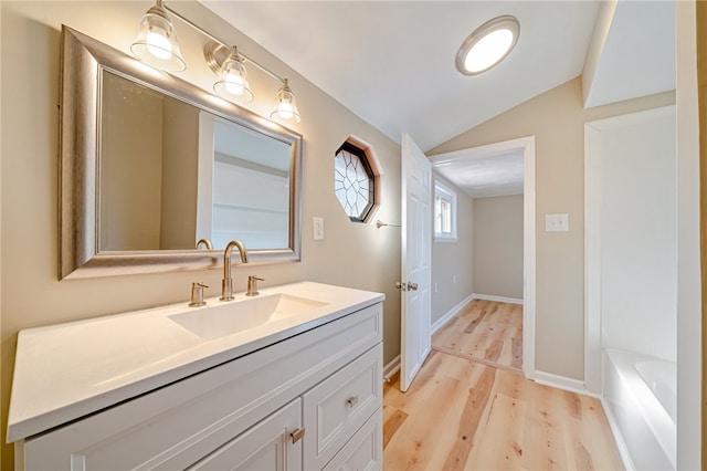 bathroom with vanity, vaulted ceiling, wood-type flooring, and a washtub