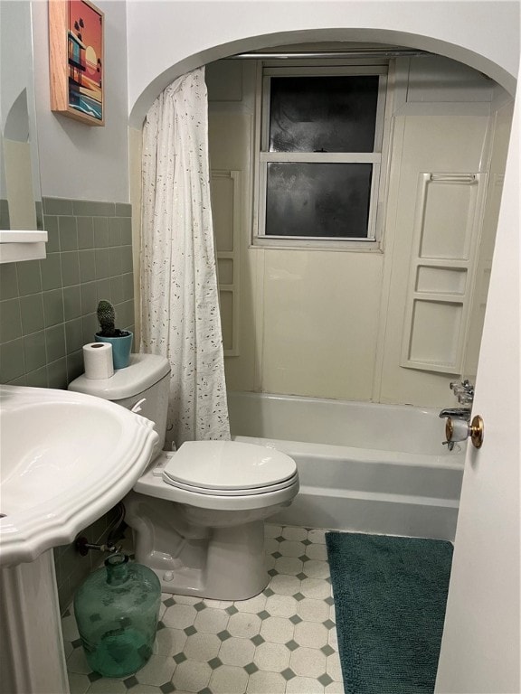 bathroom with tile walls, shower / tub combo with curtain, and toilet