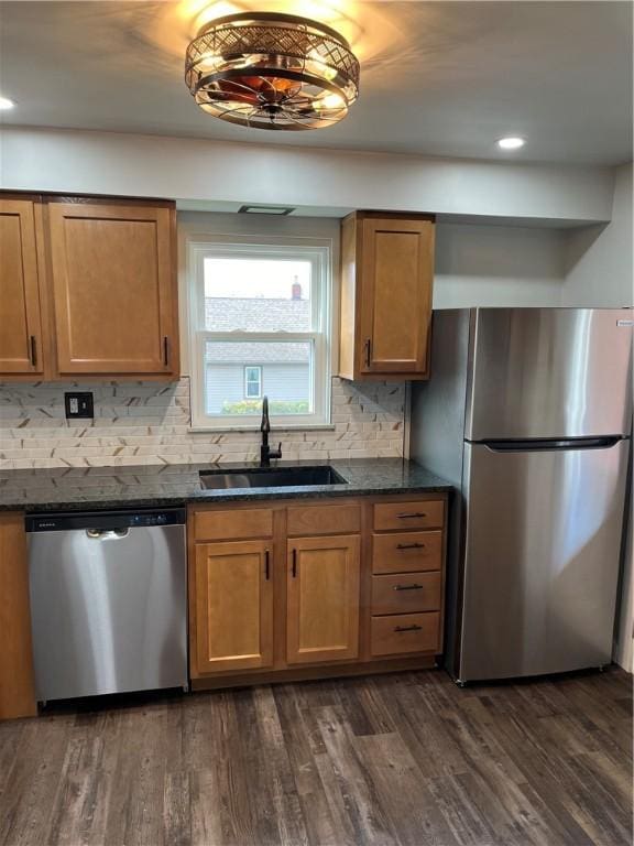 kitchen with stainless steel appliances, sink, backsplash, dark stone counters, and dark wood-type flooring