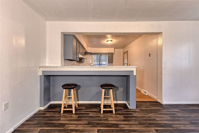 kitchen with gray cabinets, kitchen peninsula, a breakfast bar area, and dark hardwood / wood-style flooring