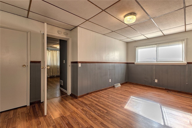 empty room with a drop ceiling, wood-type flooring, and wood walls