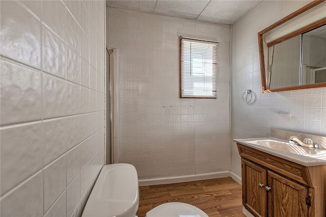 bathroom featuring wood-type flooring, toilet, walk in shower, tile walls, and vanity