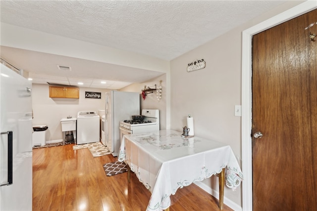 kitchen with white appliances, washer / clothes dryer, sink, light wood-type flooring, and a textured ceiling