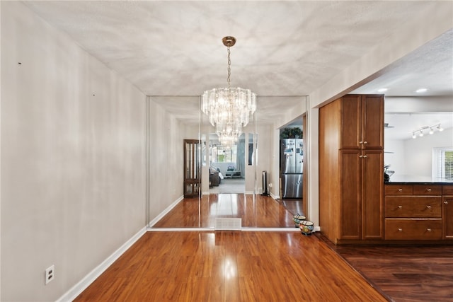 unfurnished dining area with a textured ceiling, an inviting chandelier, and dark hardwood / wood-style flooring