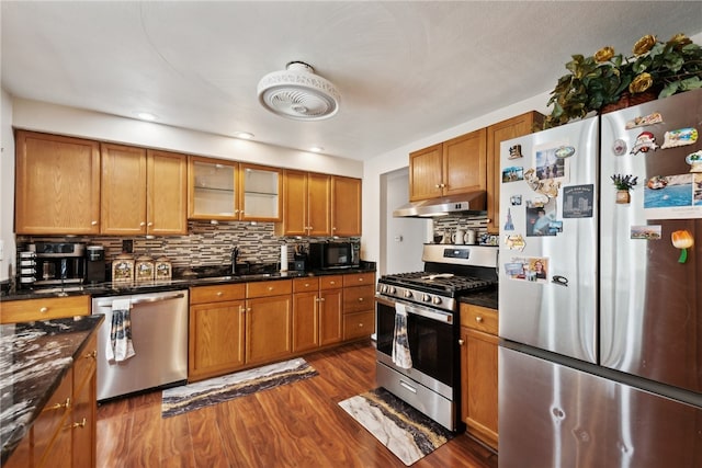 kitchen featuring sink, dark hardwood / wood-style flooring, stainless steel appliances, dark stone countertops, and decorative backsplash