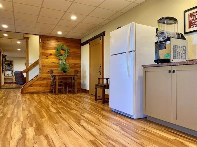 kitchen with light wood-type flooring, a drop ceiling, white refrigerator, and a barn door