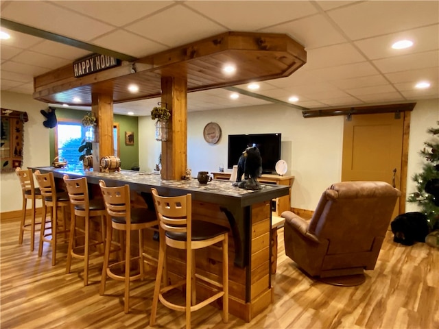 bar featuring a barn door, light hardwood / wood-style flooring, and a drop ceiling