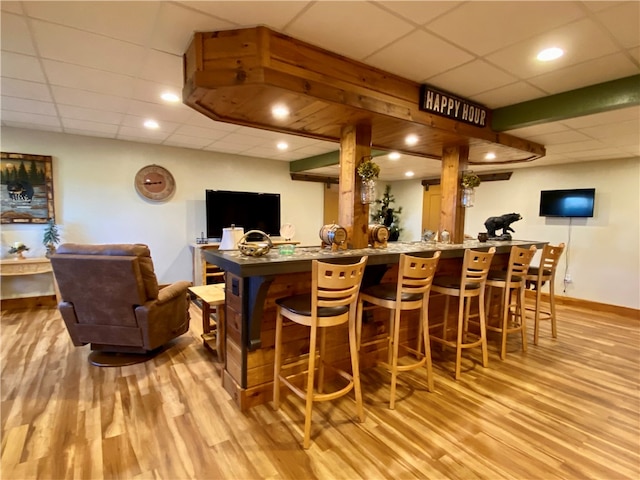 bar featuring a drop ceiling and light hardwood / wood-style flooring