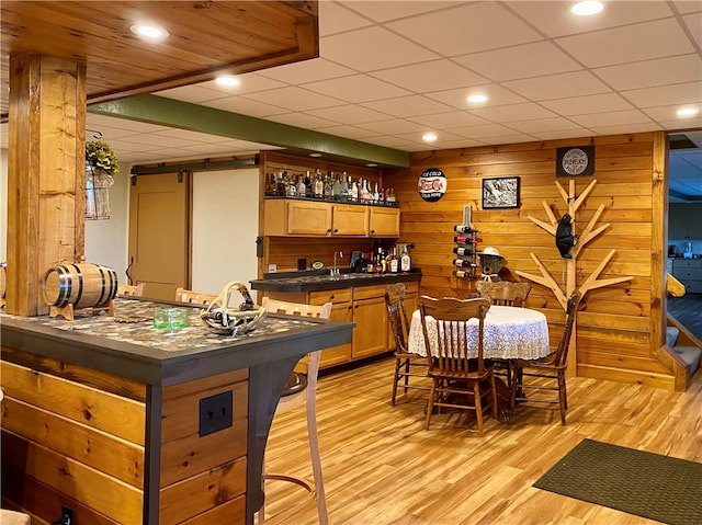 bar featuring wooden walls, light hardwood / wood-style flooring, sink, a barn door, and a paneled ceiling