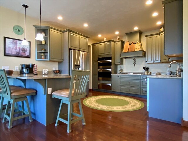 kitchen featuring a kitchen breakfast bar, dark wood-type flooring, hanging light fixtures, stainless steel appliances, and sink