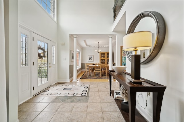 tiled entrance foyer with a towering ceiling, ornamental molding, decorative columns, and a chandelier