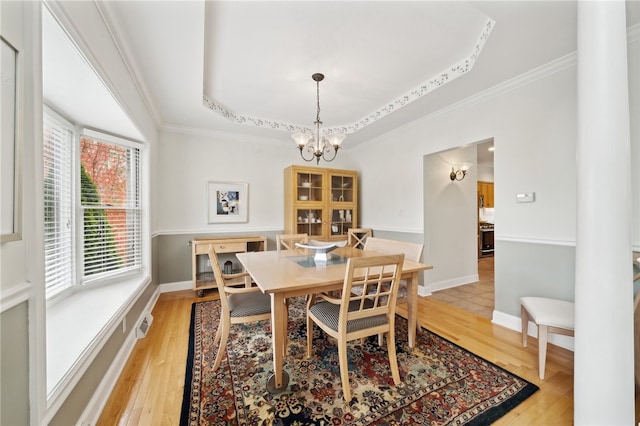 dining space with a chandelier, a tray ceiling, and light wood-type flooring