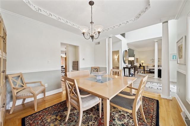 dining space featuring light wood-type flooring, a raised ceiling, decorative columns, crown molding, and an inviting chandelier