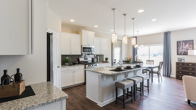 kitchen featuring appliances with stainless steel finishes, white cabinetry, decorative light fixtures, and an island with sink