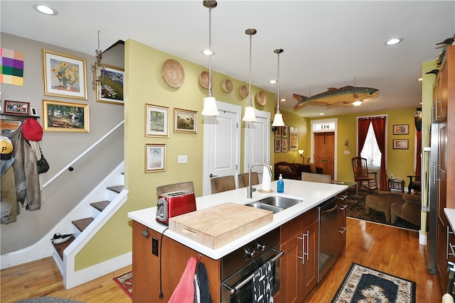 kitchen with dishwasher, hardwood / wood-style flooring, an island with sink, hanging light fixtures, and sink