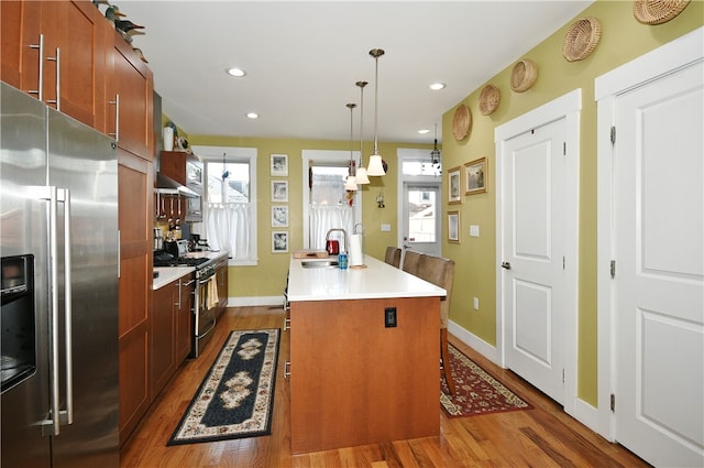 kitchen with stainless steel appliances, sink, hardwood / wood-style floors, a center island, and decorative light fixtures