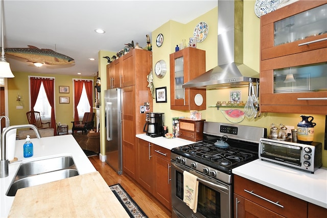 kitchen with sink, light wood-type flooring, hanging light fixtures, stainless steel appliances, and wall chimney exhaust hood