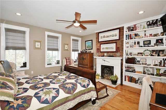 bedroom featuring a large fireplace, light hardwood / wood-style floors, and ceiling fan