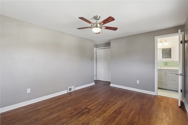 unfurnished bedroom featuring a closet, ensuite bath, dark wood-type flooring, and ceiling fan