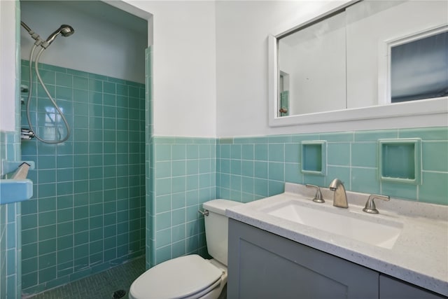 bathroom featuring toilet, vanity, a tile shower, and tile walls